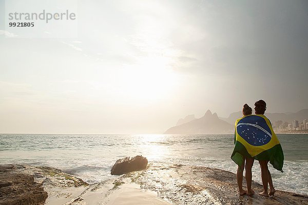 Rückansicht von zwei jungen Frauen in brasilianischer Flagge am Strand von Ipanema  Rio De Janeiro  Brasilien