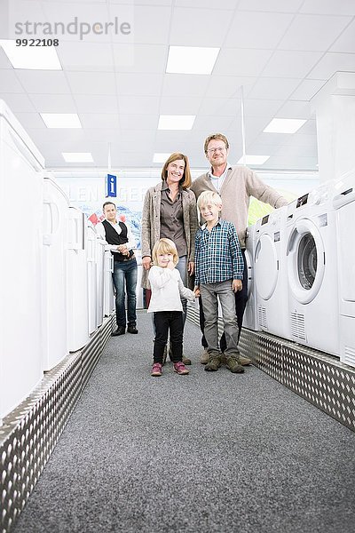 Porträt einer Familie mit zwei Kindern beim Durchstöbern von Waschmaschinen im Elektronikgeschäft