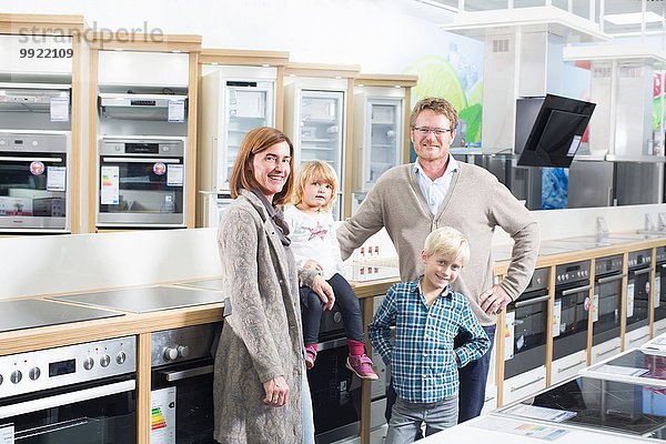 Porträt der Familie mit zwei Kindern beim Durchstöbern von Kochfeldern im Elektronikgeschäft