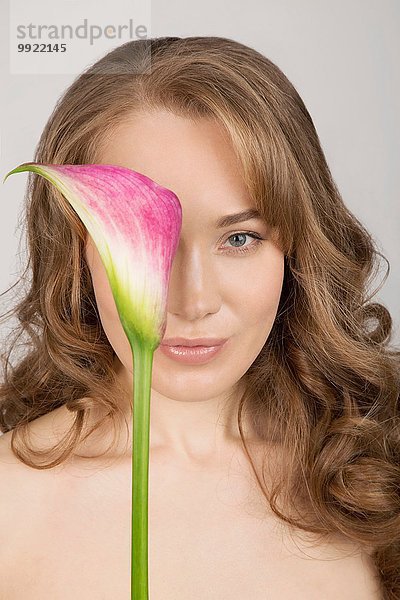 Porträt einer jungen Frau  die eine Blume im Gesicht hält.
