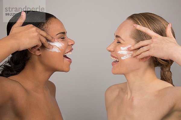 Porträt von zwei jungen Frauen  die Schönheitscreme auf das Gesicht auftragen.