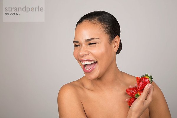Porträt einer jungen Frau  lachend  mit einer Handvoll Erdbeeren in der Hand.