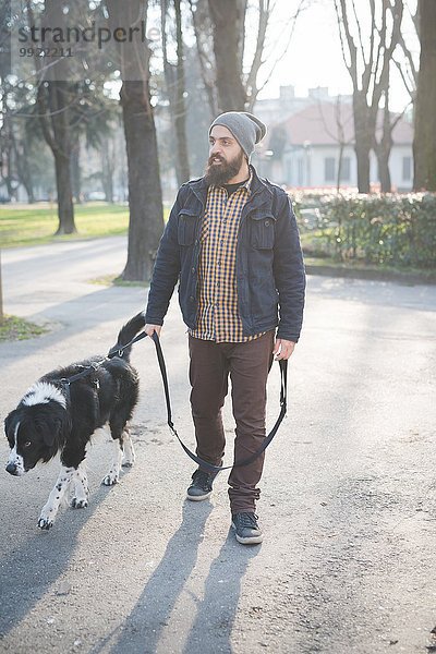 Mittlerer erwachsener Mann geht mit Hund durch den Park