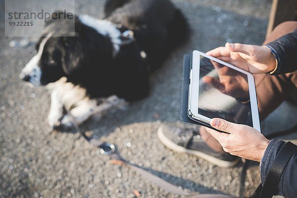 Mittlerer erwachsener Mann  im Freien mit Hund sitzend  mit digitalem Tablett  Konzentration auf die Hände