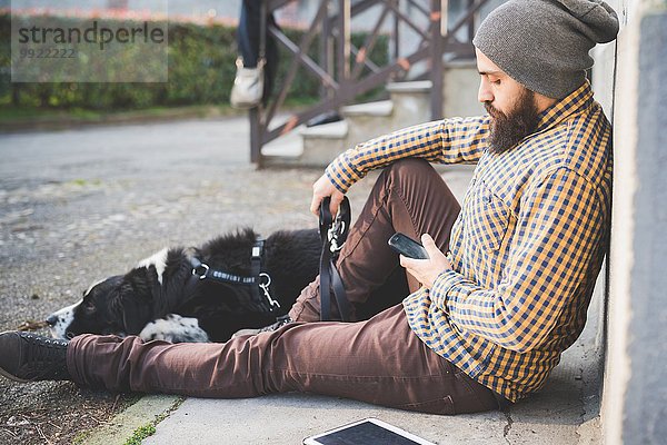 Mittlerer Erwachsener Mann  der mit Hund im Freien sitzt  mit Smartphone