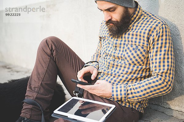 Mittelgroßer Mann im Freien mit Hund  mit Smartphone und Digital-Tablett