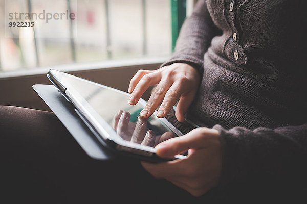 Junge Frau am Fenster sitzend  mit digitalem Tablett  Konzentration auf die Hände