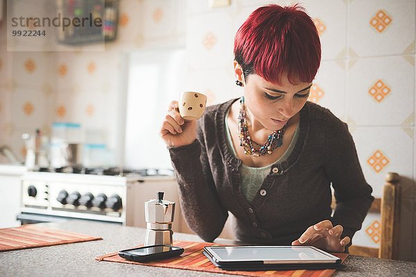 Junge Frau  die am Tisch sitzt und Kaffee trinkt  mit Hilfe eines digitalen Tabletts.
