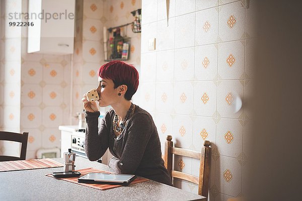 Junge Frau sitzt am Tisch und trinkt Kaffee.