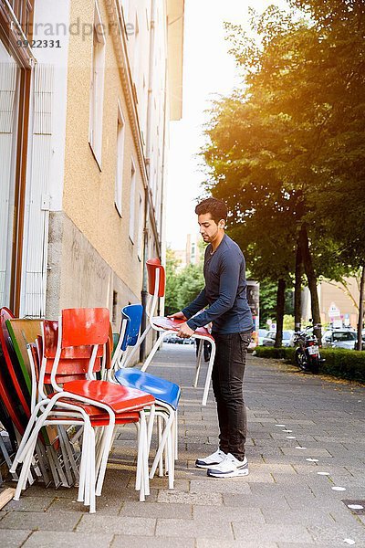 Junger Mann  Stühle ausstellen  Außengebäude