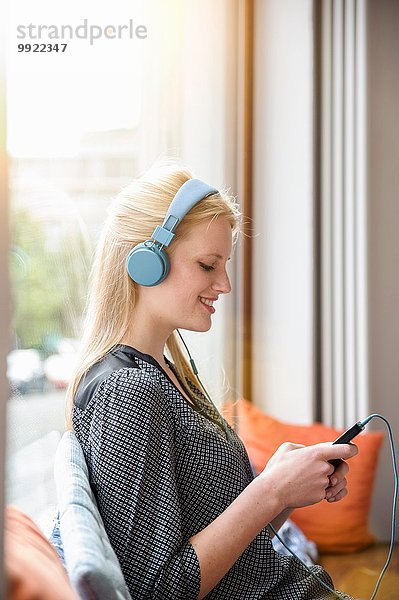 Junge Frau  Kopfhörer tragend  im Café sitzend  Smartphone haltend