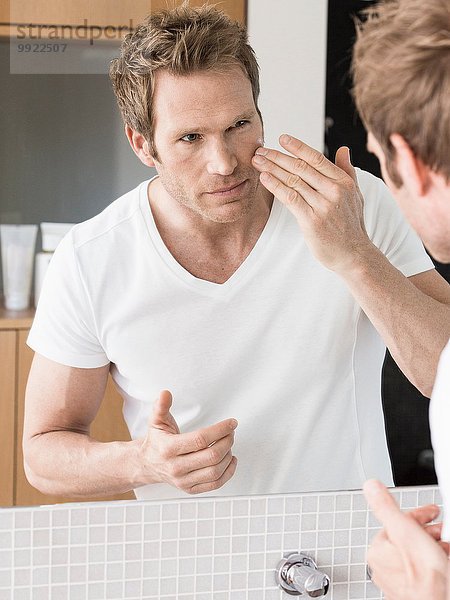 Mittlerer Erwachsener Mann  der in den Badezimmerspiegel schaut  der Gesicht Creme anwendet