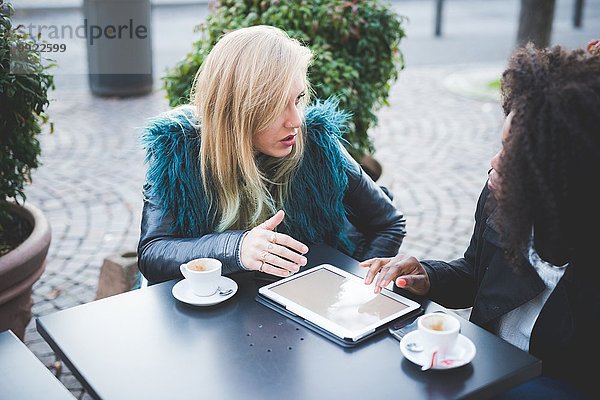 Zwei junge Frauen  die ein digitales Tablett im Straßencafé  Comer See  Comer See  Italien  benutzen.