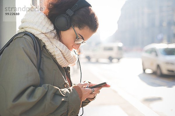 Junge Frau mit Kopfhörer wählt Smartphone-Musik auf der Straße