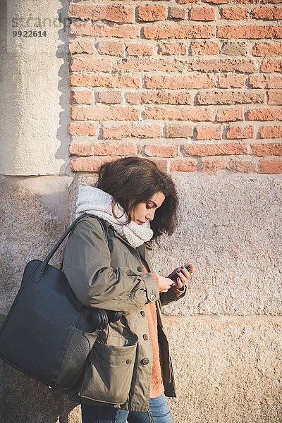 Junge Frau  die sich an die Wand lehnt und Smartphone-Texte liest.