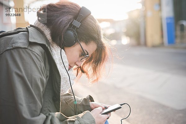 Junge Frau sitzt auf dem Bürgersteig und liest Smartphone-Texte.