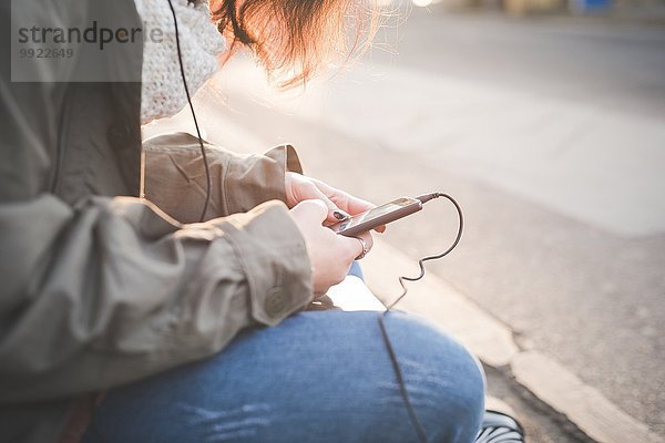 Ausschnitt einer jungen Frau  die auf dem Bürgersteig sitzt und Smartphone-Texte liest.