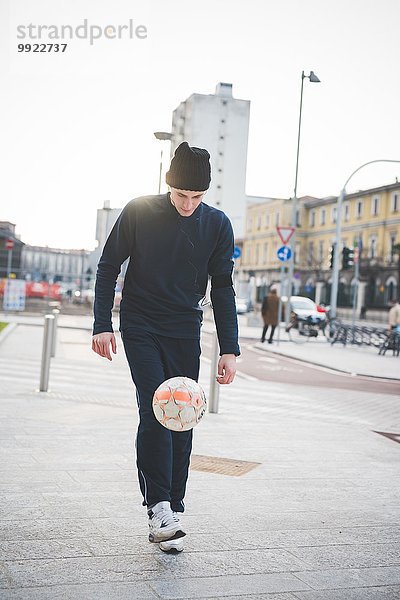 Junger männlicher Fußballspieler spielt Keepy Uppy auf der City Street