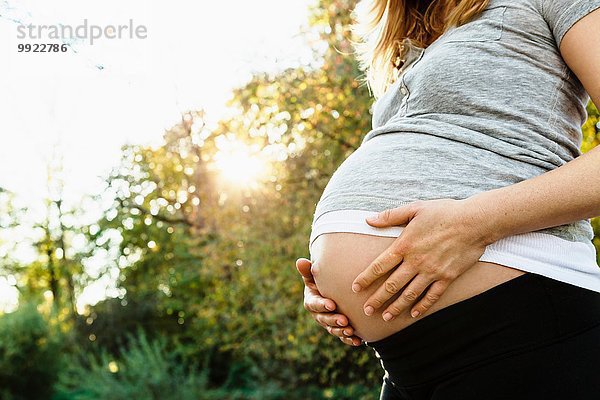 Schwangere Frau hält Bauch  im Freien  Mittelteil