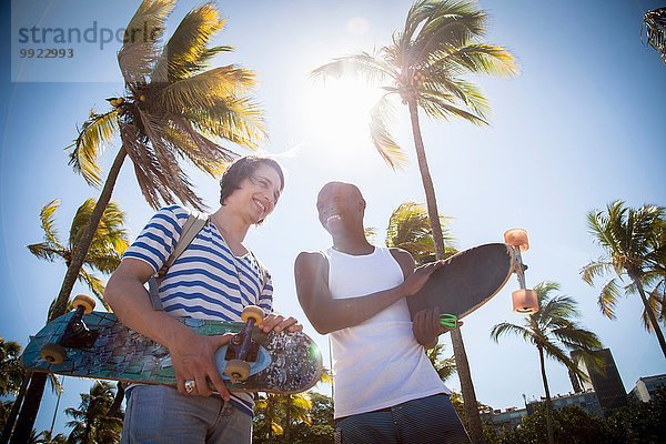 Zwei Männer  die Skateboards in der Hand halten und im Freien spazieren gehen