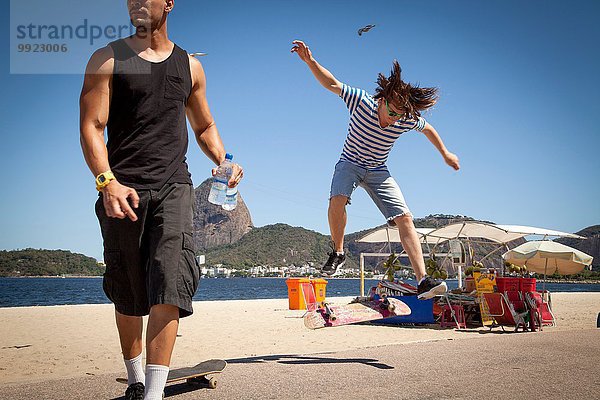 Junger Mann springt auf dem Skateboard  während der Freund wegguckt.