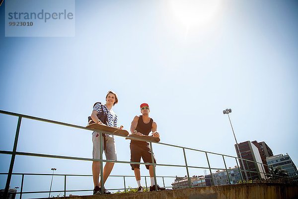 Zwei Männer  die Skateboards halten  sich auf Geländer lehnen  Blickwinkel niedrig