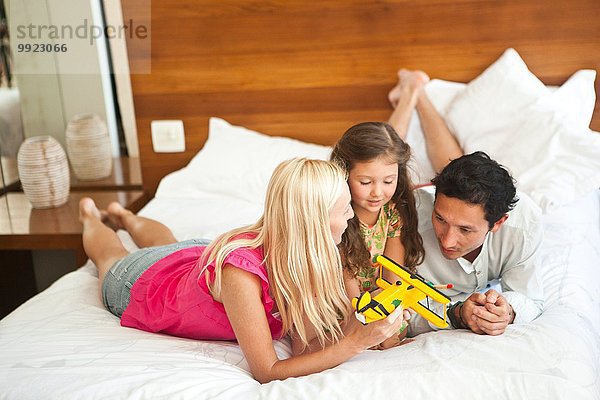 Junge Familie auf dem Bett liegend  spielend mit dem Spielzeugflugzeug