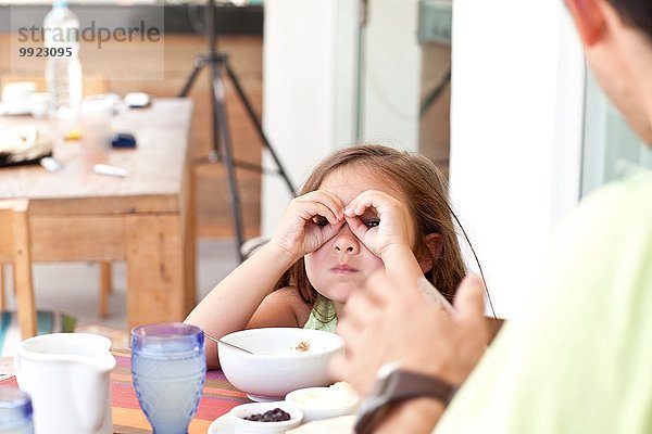 Vater und Tochter sitzen am Frühstückstisch  Tochter macht Fernglas aus den Fingern