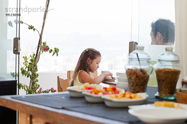 Vater und Tochter sitzen am Frühstückstisch auf dem Balkon  gesundes Essen im Vordergrund