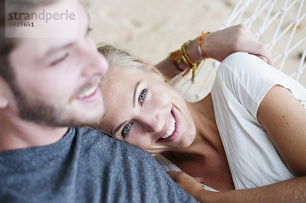 Nahaufnahme eines lächelnden jungen Paares auf einer Strandhängematte
