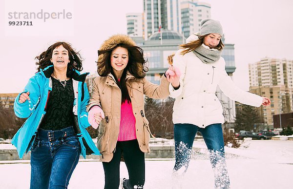 Drei junge Frauen  die im Schnee laufen und Händchen halten.