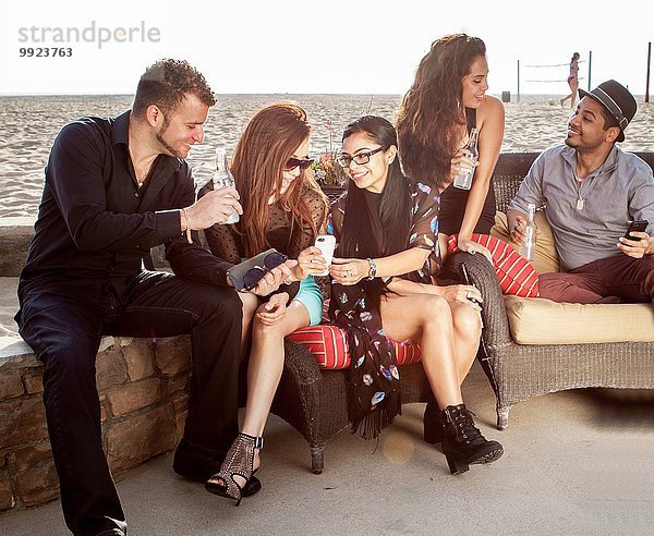 Gruppe von Freunden an einer Strandbar  die sich unterhalten und Smartphones anschauen