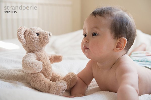 Vorne liegender Babyjunge mit Teddybär neben ihm