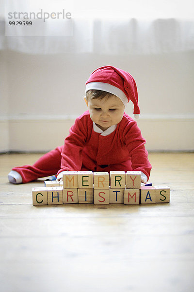 Ein kleiner Junge  der als Weihnachtsmann verkleidet ist  mit Spielzeugblöcken  in denen er Frohe Weihnachten liest.