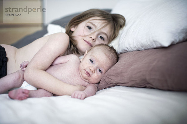 Kleines Mädchen auf dem Bett liegend mit kleinem Bruder
