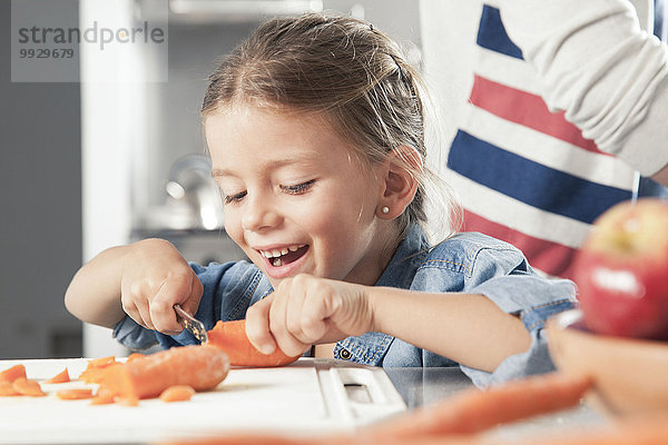 Kleines Mädchen beim Schneiden von Karotten in der Küche