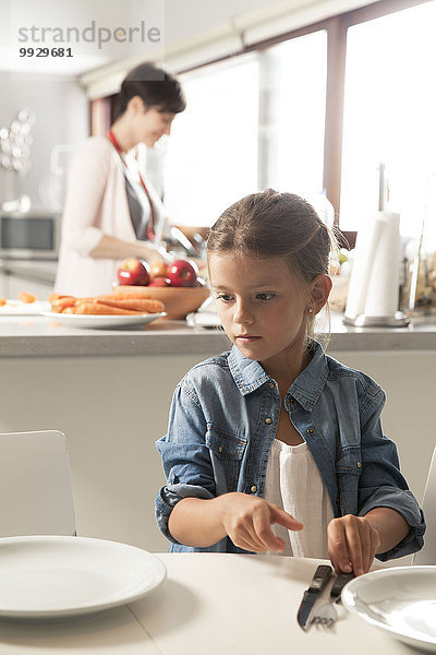Mädchen beim Tischdecken  Mutter beim Essen im Hintergrund