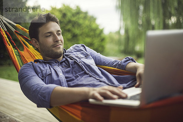 Mann in Hängematte liegend mit Laptop-Computer