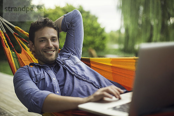 Mann in Hängematte liegend mit Laptop-Computer