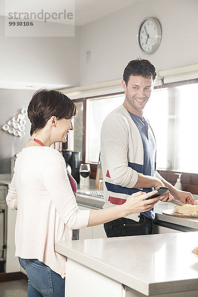 Paar  das zusammen auf das Smartphone schaut  während es Essen in der Küche zubereitet.