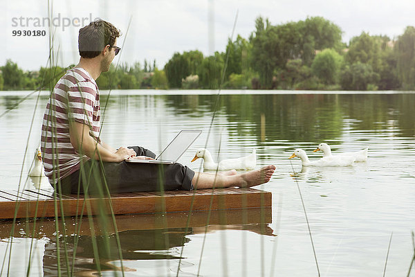 Mann sitzt auf dem Dock mit dem Laptop