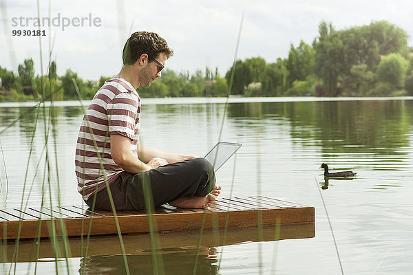 Mann sitzt auf dem Dock mit dem Laptop