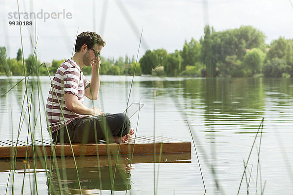 Mann mit Laptop-Computer auf dem Dock während des Gesprächs auf dem Handy