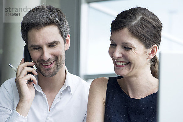 Geschäftskollegen lächeln zusammen  Mann spricht am Handy