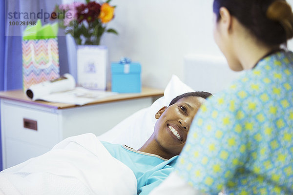 Lächelnder Patient im Krankenhausbett lächelt Krankenschwester an