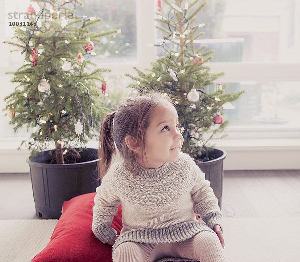 Lächelndes Mädchen vor Topfbäumen mit Weihnachtsbeleuchtung