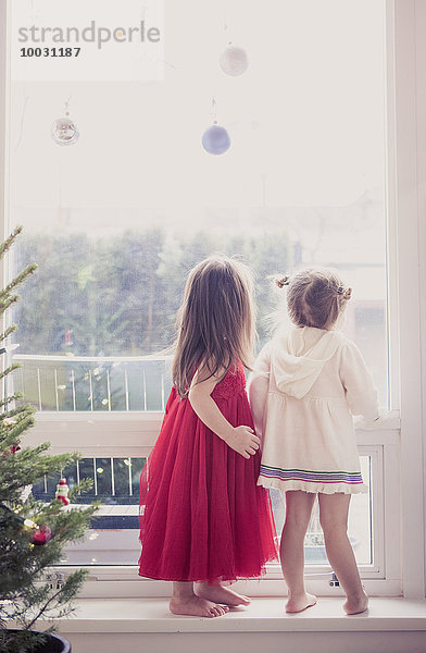 Mädchen auf Fensterbank unter Weihnachtsschmuck