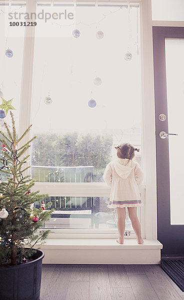 Neugieriges Mädchen auf Fensterbank unter dem Weihnachtsschmuck