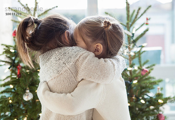 Mädchen umarmen sich vor Weihnachtsbäumen