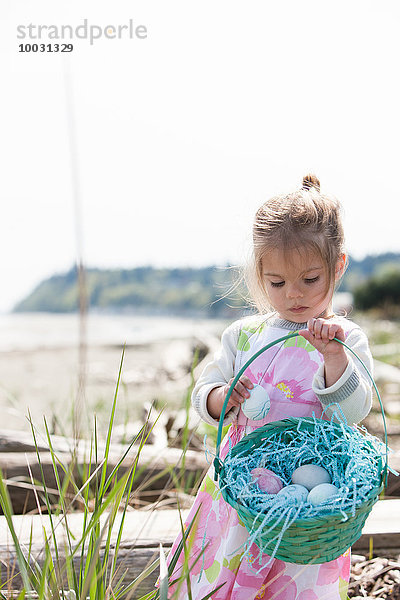 Mädchen sammelt Ostereier im Korb am Strand